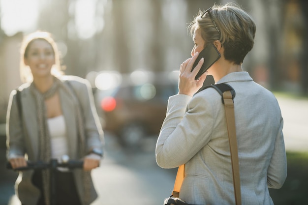 仕事に行くときにスマートフォンを使用して成熟したビジネス女性の背面図。