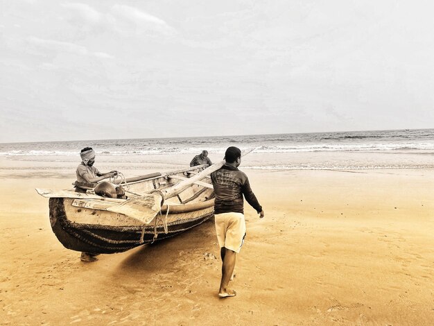 Rear view of men on beach against sky