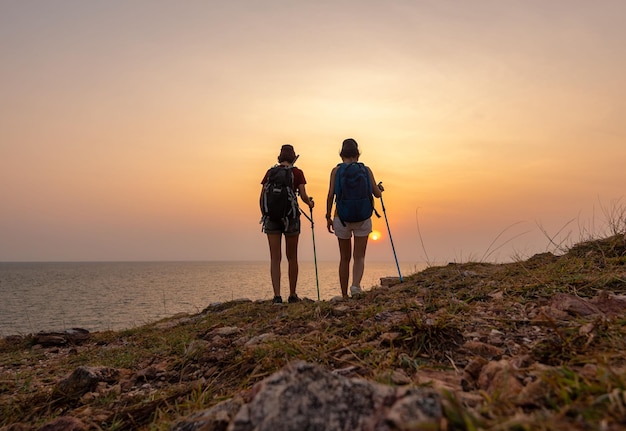 Rear view of men standing on shore against sky during sunset