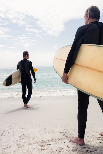 Rear view of men walking on the beach with surfboard