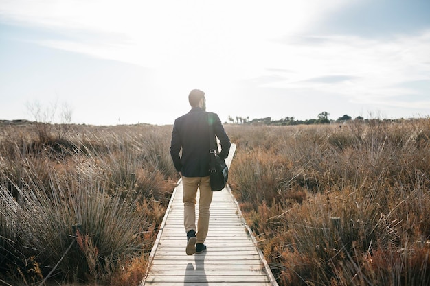 Rear view of mid adult man walking on boardwalk against sky