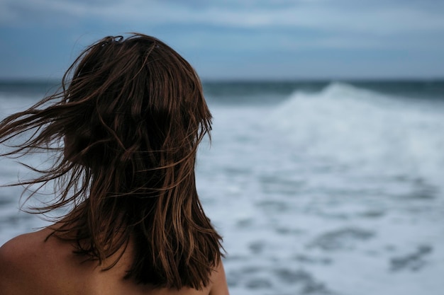 rear view of mid adult woman standing at beach against cloudy sky