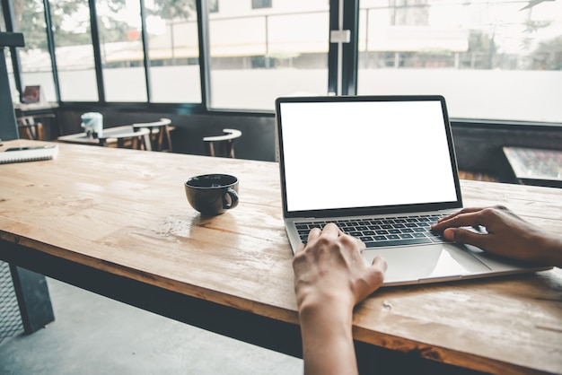 Rear view mockup image of a woman's hand working on a laptop with blank white desktop copy space screen on a desk