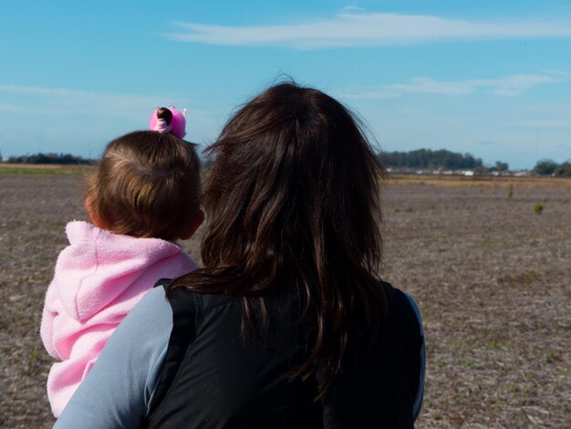 Foto vista posteriore di una madre che porta la figlia contro il cielo