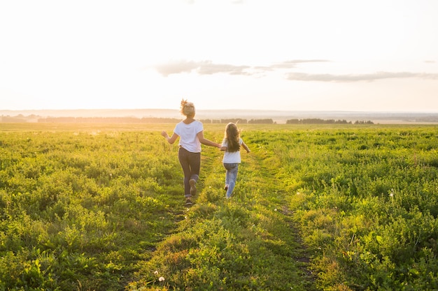 Rear view of mother and daughter running in green field with sunset