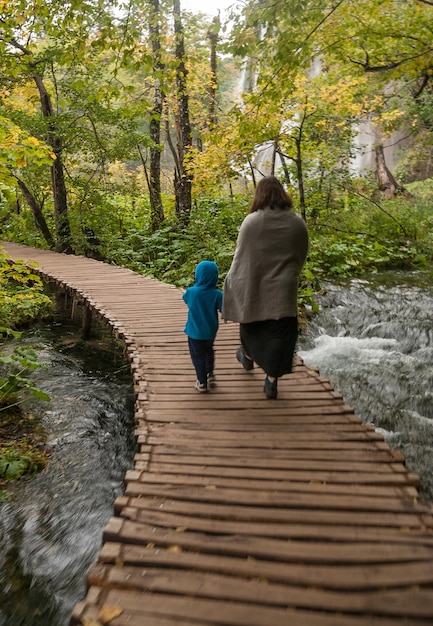 Photo rear view of mother and son walking on boardwalk over stream in forest