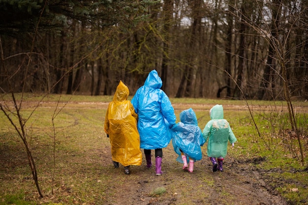 Rear view of mother and three children walking in the forest after rain in raincoats together