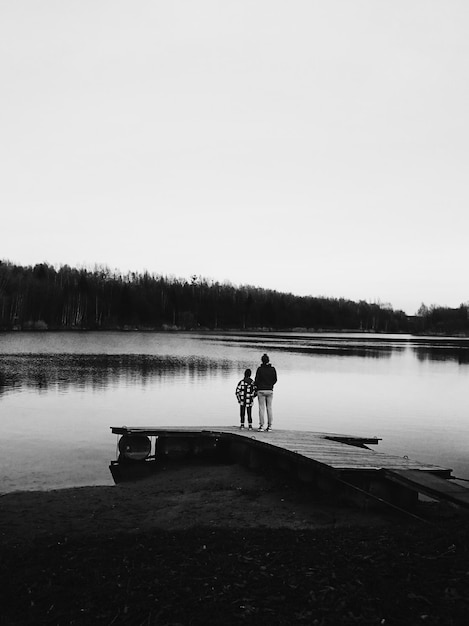 Photo rear view of mother with daughter standing by lake against clear sky