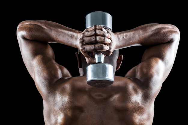 Rear view of muscular man lifting dumbbell behind head