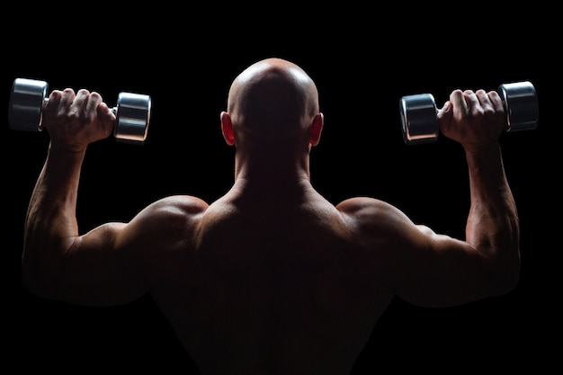 Retrovisione dell'uomo muscolare che alza i dumbbells