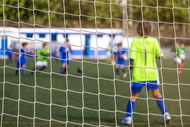 Foto retrovisione dietro la rete di un portiere di calcio del bambino nell'obiettivo. sfoca lo sfondo