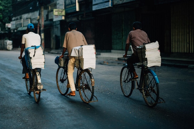 Rear view of newspaper vendors riding bicycles on road in city