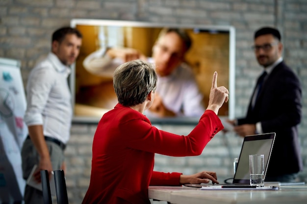 Вид сзади на деловую женщину, поднимающую руку, чтобы задать вопрос во время деловой встречи в офисе