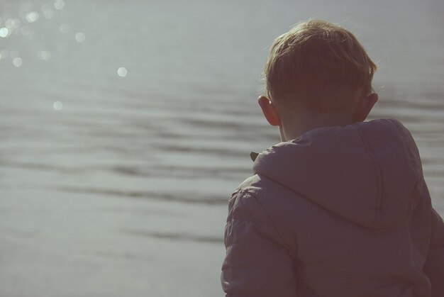Фото Задний вид мальчика у озера в солнечный день.