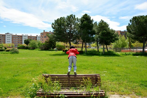 写真 植物で満たされたベンチで公園で遊んでいる男の子の後ろの景色