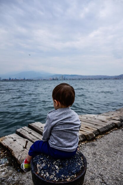 写真 空の反対側の海に座っている少年の後ろの景色