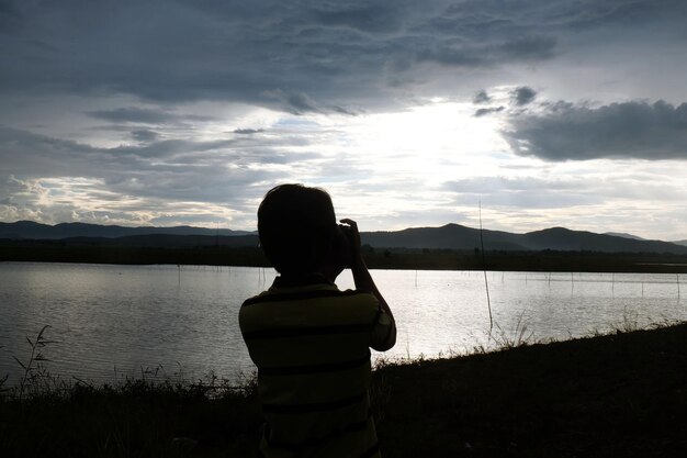 写真 空に向かって湖のそばに立っている男の子の後ろの景色