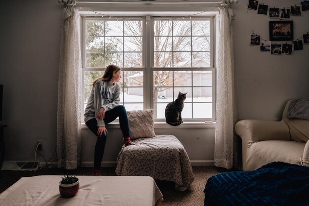 写真 窓から眺める少女と彼女の猫の後ろの景色