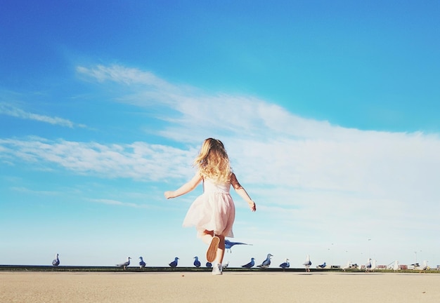 写真 空の反対側の鳥に沿ってビーチで走っている女の子の後ろの景色