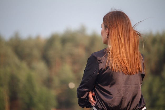 Фото Вид сзади девушки с длинными рыжими волосами, девушка смотрит на лес, выборочный фокус