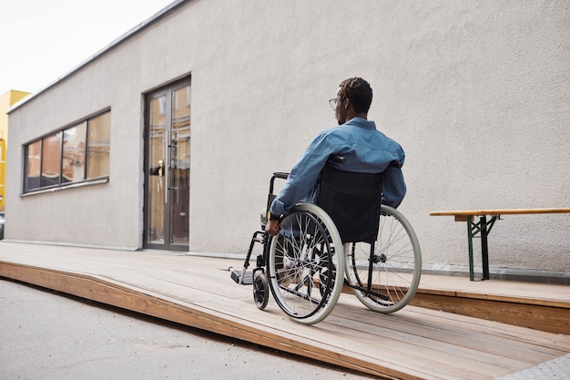 사진 그의 집 입구에 지어진 휠체어 경사로를 사용하여 캐주얼 셔츠를 입은 장애인 아프리카계 미국인 남자의 후면보기