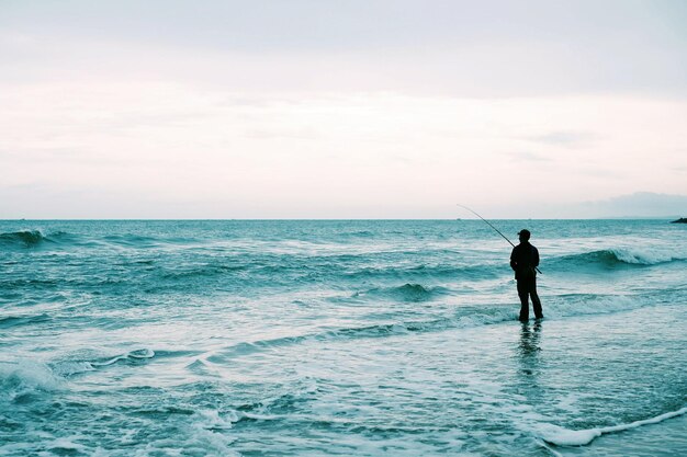 写真 海岸で釣りをしている男の後ろの景色