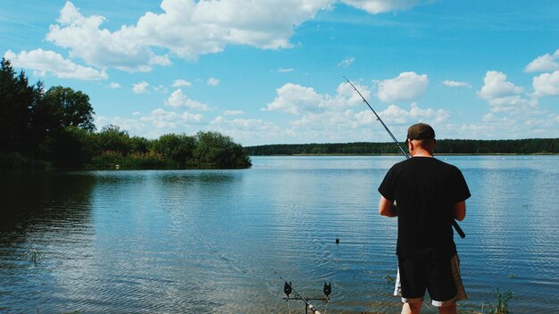 写真 空を背景に湖で釣りをしている男の後ろの景色