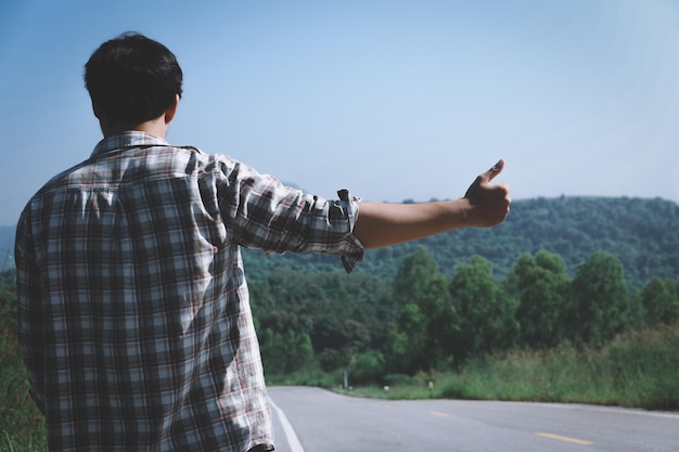 写真 田舎の道路でヒッチハイクをしている男の後ろの景色