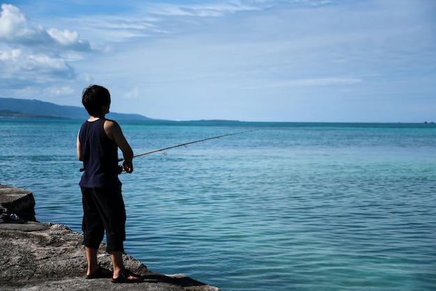 写真 海で釣りをしている男の後ろの景色