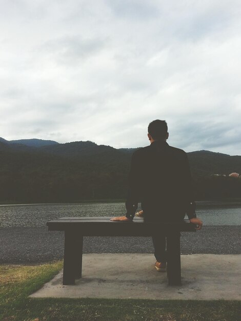 写真 空に照らして湖のそばに座っている男の後ろの景色