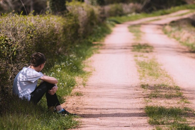 写真 畑の真ん中に歩道に座っている男の後ろの景色