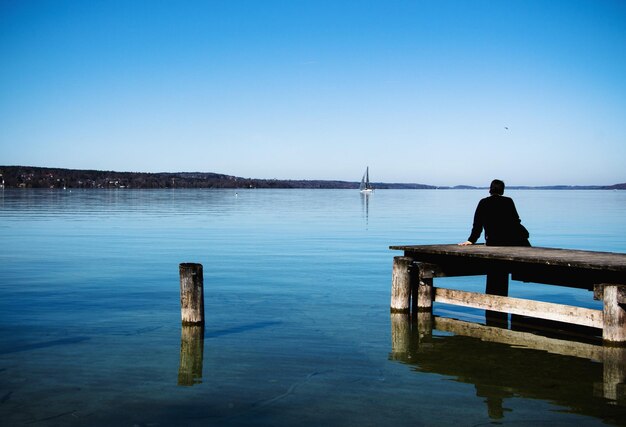 写真 澄んだ空の前で湖の上の<unk>に座っている男の後ろの景色