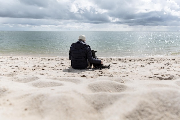 写真 空の向こうのビーチで犬と一緒に座っている男の後ろの景色