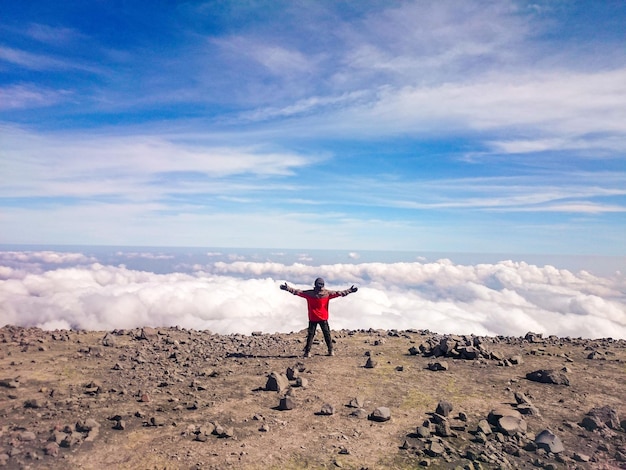 写真 雲の空を背景に崖の上に立っている男の後ろの景色