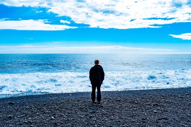 写真 空に照らしてビーチに立っている男の後ろの景色