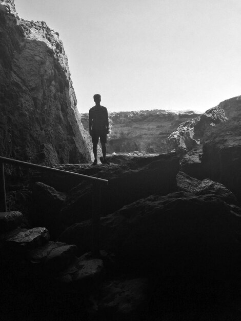 Фото Задний вид человека, стоящего на скале на фоне ясного неба