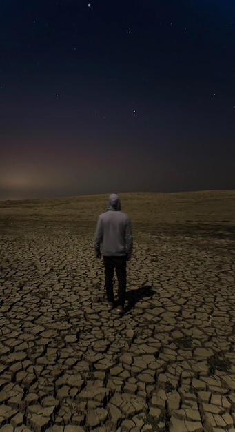 Фото Задний вид человека, стоящего на треснувшем поле на фоне звездного поля
