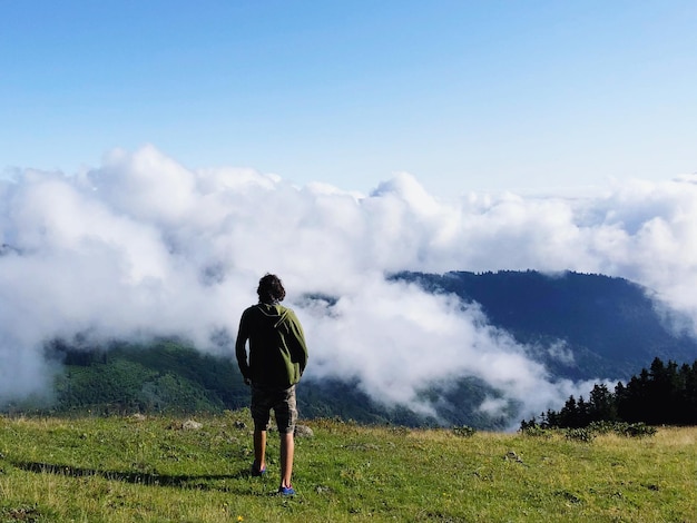 写真 雲の空を背景に山の上に立っている男の後ろの景色