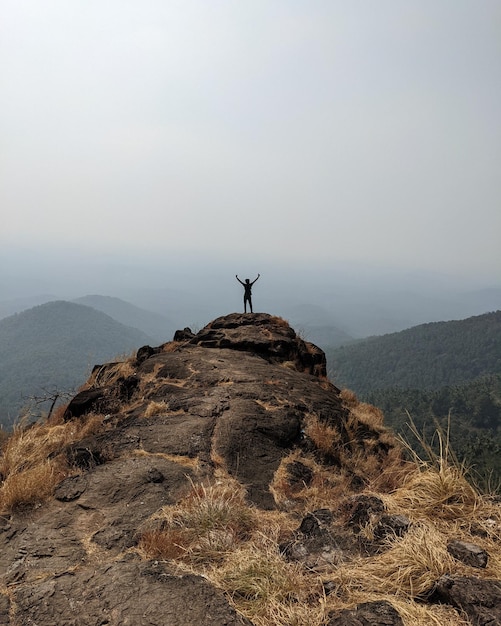Фото Задний вид человека, стоящего на горе на фоне неба