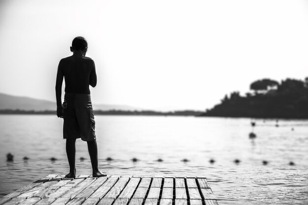 写真 空に向かって湖の上の埠頭に立っている男の後ろの景色