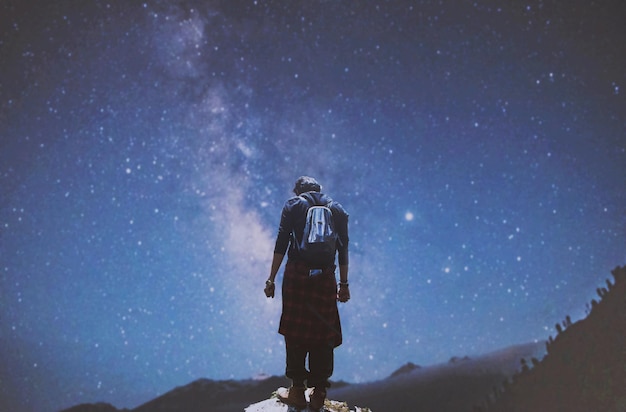 写真 夜空を背景に岩の上に立っている男の後ろの景色