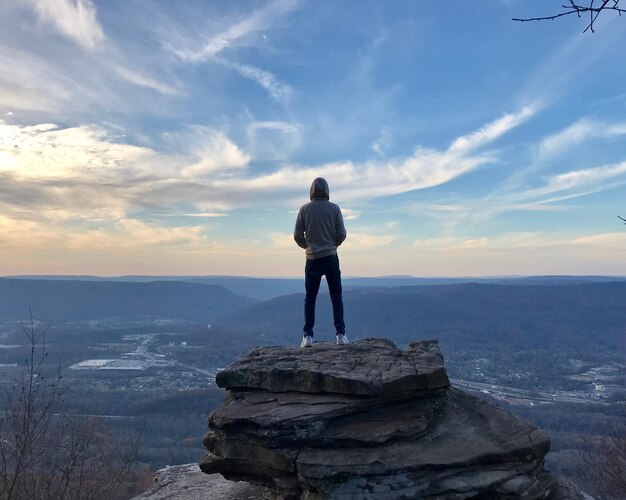 写真 天空を背景に岩層の上に立っている男の後ろの景色