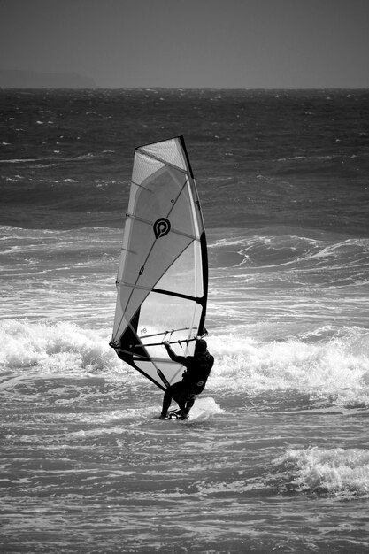 写真 海でウィンドサーフィンをしている男の後ろの景色