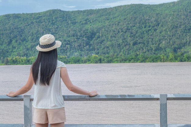 写真 山の反対側のレールに立って湖を見ている中年女性の後ろの景色