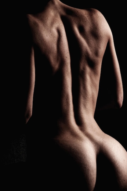 写真 黒い背景に立っている裸の女性の後ろの景色