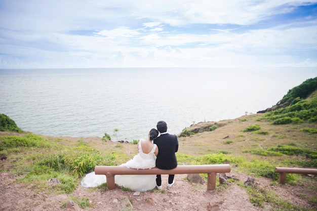 사진 새로 결혼 한 부부 가 하늘 을 배경 으로 해변 에 앉아 있는 뒷면