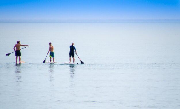 写真 青い空を背景に海でパドルボードをしている男性の後ろの景色