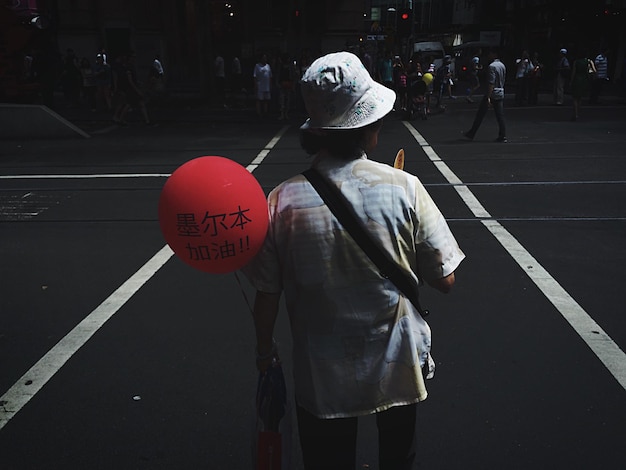 Фото Задний вид человека, держащего красный воздушный шар на улице