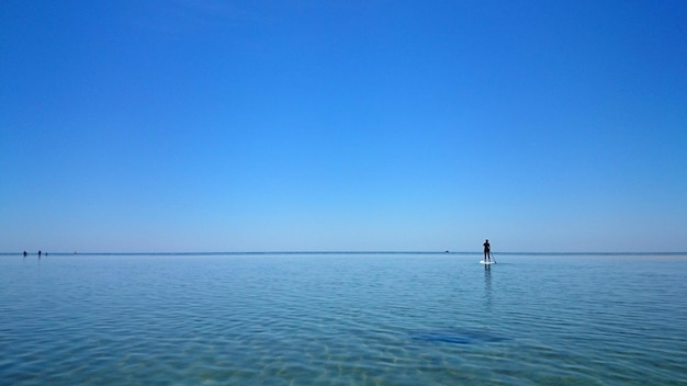 写真 海でパドルボードをしている人の後ろの景色