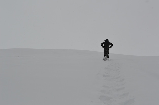 Фото Задний вид человека, идущего по покрытому снегом полю зимой